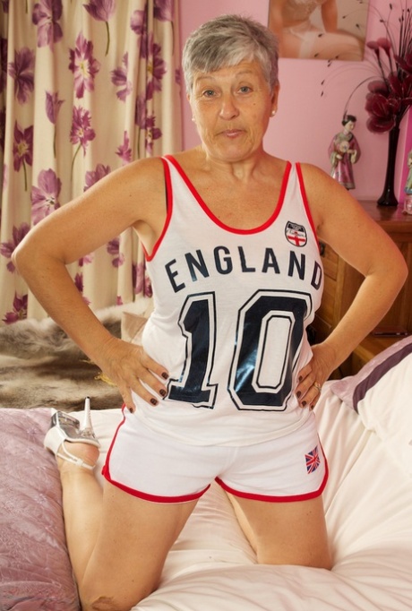Short haired UK granny Savana uncovers her large tits on a bed in a thong
