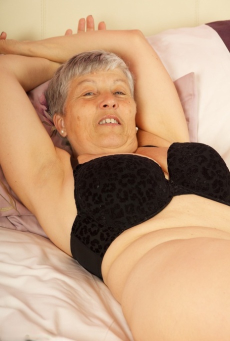 Short haired UK granny Savana uncovers her large tits on a bed in a thong