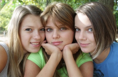 Three young looking girls gets naked on a wooden bench in the countryside