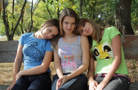 Three young looking girls gets naked on a wooden bench in the countryside